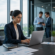 Businesswoman working on a laptop while colleagues talk in the background