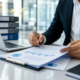 Business professional reviews financial charts while signing documents at an office desk