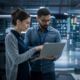 Two IT professionals reviewing data on a laptop in a modern server room
