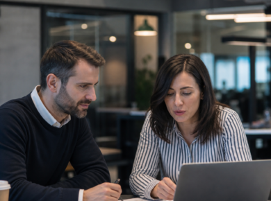 Two colleagues review supplier corrective action documents on a laptop in a modern office.